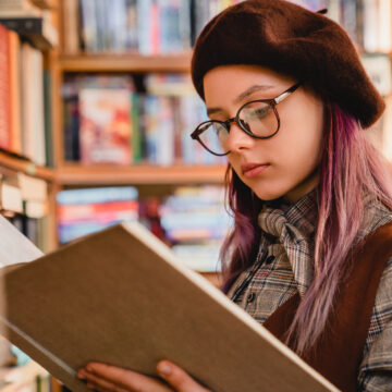 Intelligent young caucasian girl in glasses reading a book at the library Reading Habit: 6 Tips To Develop a Reading Habit