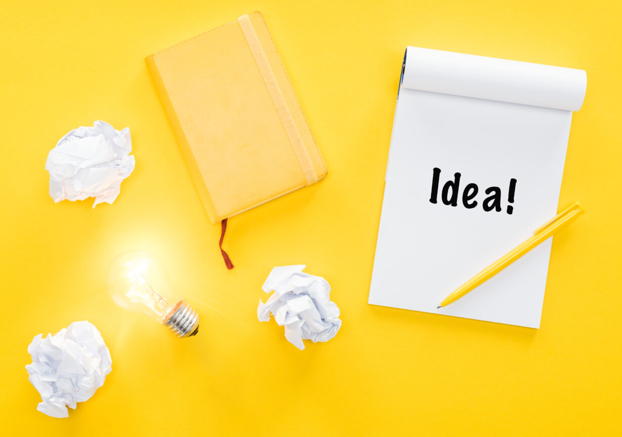 notebook with 'idea' word, crumbled paper balls and glowing light bulb, having new ideas concept Barriers to Becoming an Effective Writer