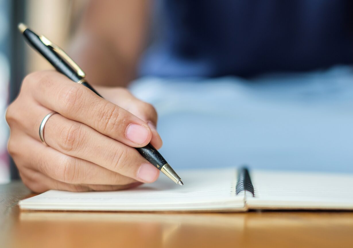 Businesswoman writing something on notebook in office, hand of w How to Improve Your Writing: 8 Tips