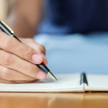 Businesswoman writing something on notebook in office, hand of w How to Improve Your Writing: 8 Tips
